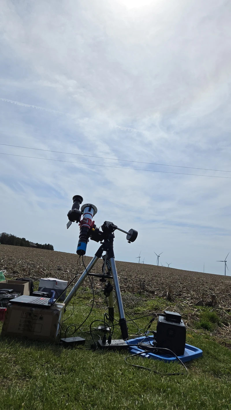 Telescope on an equatorial mount set up in a farm field near Lake Erie, wind turbines on the horizon